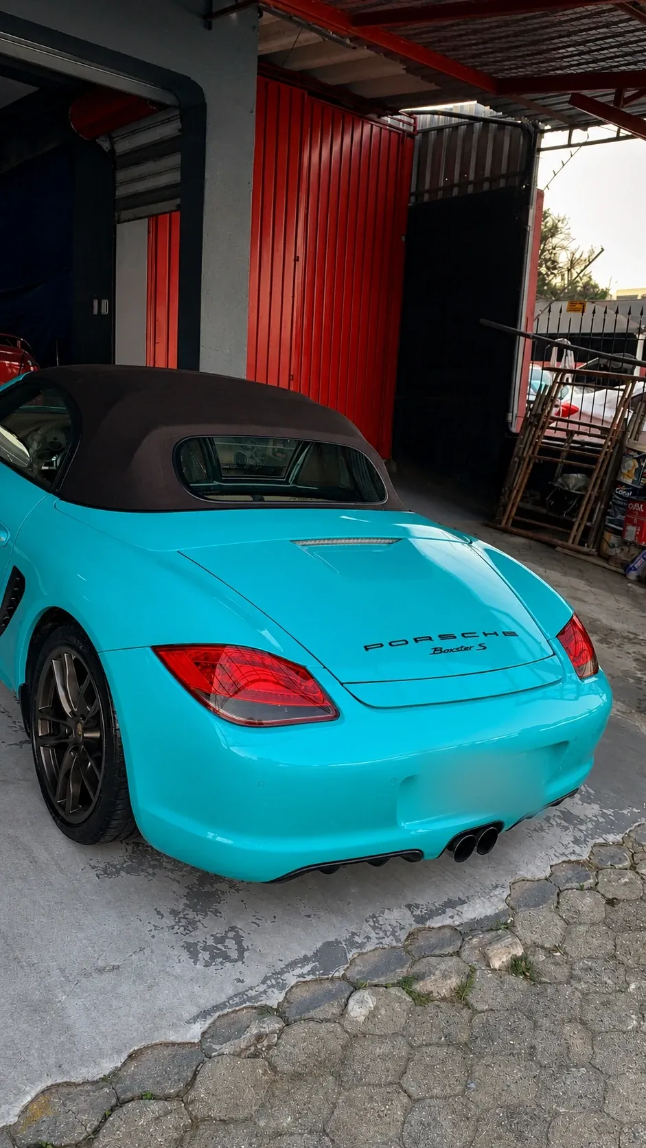 Porsche Boxster azul-turquesa estacionado na entrada da oficina da RM