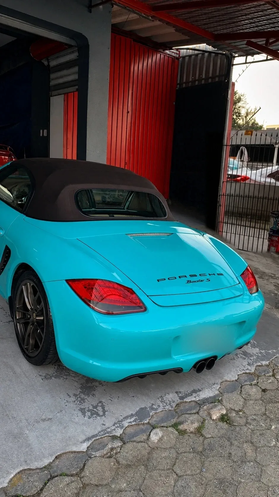 Porsche Boxster azul-turquesa estacionado na entrada da oficina da RM