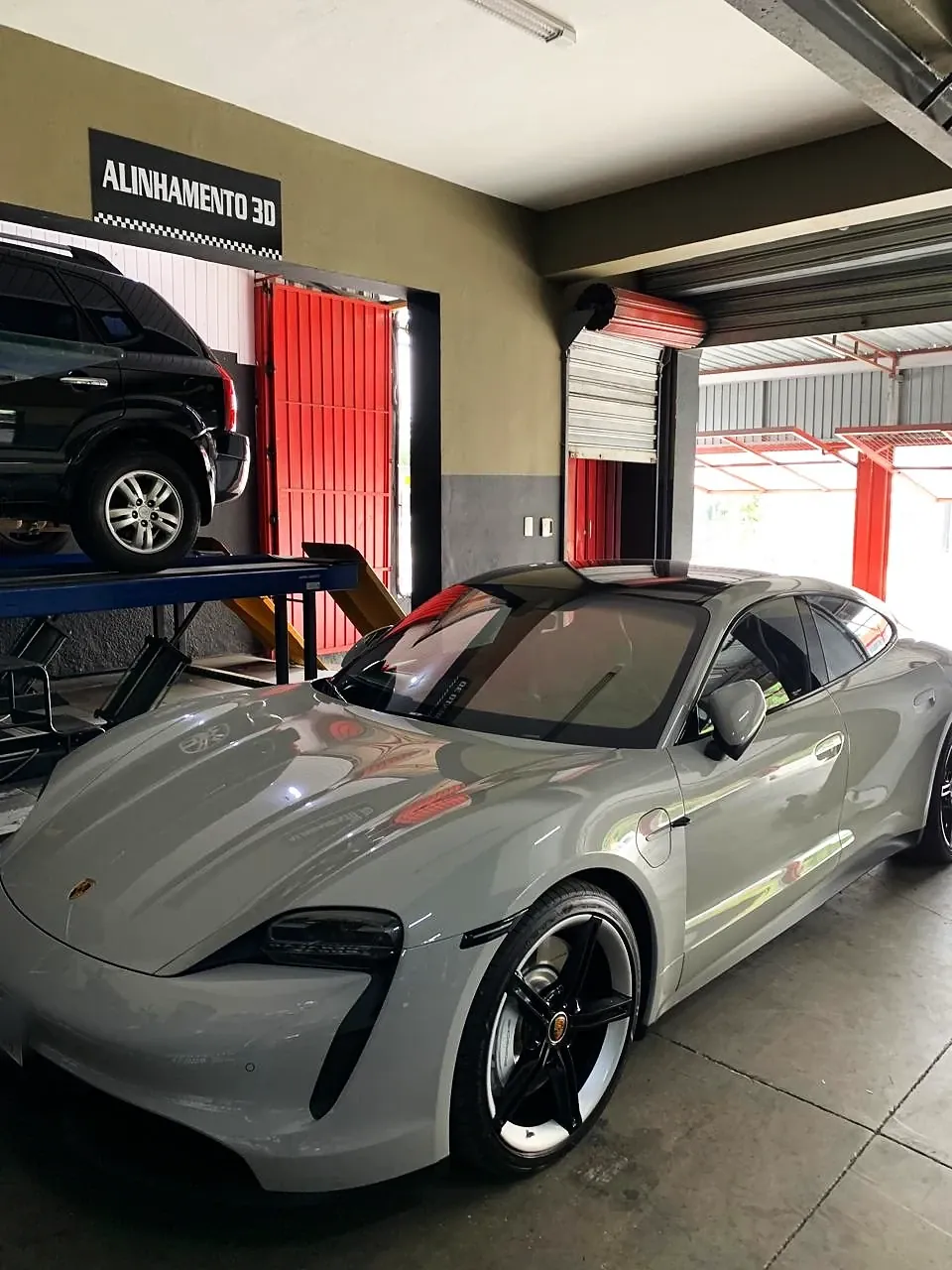 Porsche Taycan cinza na entrada da oficina, junto à placa de alinhamento 3D